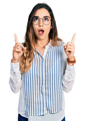 Wall Mural - Beautiful hispanic woman wearing casual striped shirt amazed and surprised looking up and pointing with fingers and raised arms.