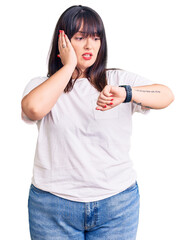 Poster - Young plus size woman wearing casual clothes looking at the watch time worried, afraid of getting late