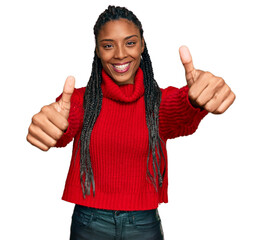 African american woman wearing casual winter sweater approving doing positive gesture with hand, thumbs up smiling and happy for success. winner gesture.