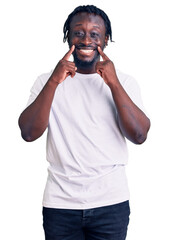 Poster - Young african american man with braids wearing casual white tshirt smiling with open mouth, fingers pointing and forcing cheerful smile