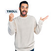 Young hispanic man with beard holding troll banner celebrating achievement with happy smile and winner expression with raised hand