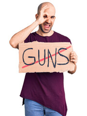 Poster - Young handsome man holding prohibited guns banner smiling happy doing ok sign with hand on eye looking through fingers