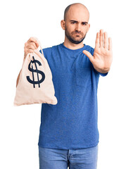 Sticker - Young handsome man holding money bag with dollar symbol with open hand doing stop sign with serious and confident expression, defense gesture