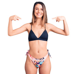 young beautiful girl wearing bikini looking confident with smile on face, pointing oneself with fing