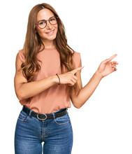 Young Hispanic Woman Wearing Casual Clothes And Glasses Smiling And Looking At The Camera Pointing With Two Hands And Fingers To The Side.