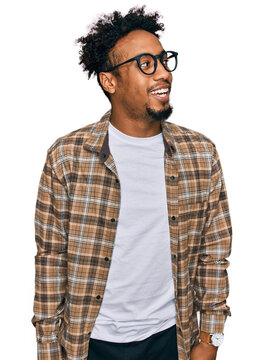 Young african american man with beard wearing casual clothes and glasses looking away to side with smile on face, natural expression. laughing confident.
