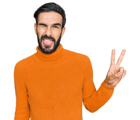 Wall Mural - Young hispanic man wearing casual clothes smiling with happy face winking at the camera doing victory sign. number two.