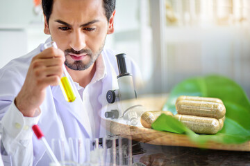 Wall Mural - scientist woman testing chemical sample in flask at laboratory with herbs capsule and herbal leaf. s