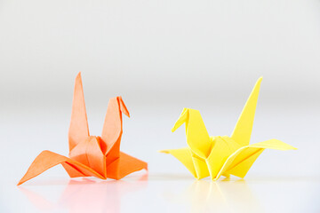 Two Japanese origami cranes facing each other, one orange, one yellow, on white background