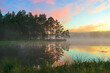 a wonderful sunrise picture with a gorgeous sky, fog covering the surface of the lake, black silhouettes of trees