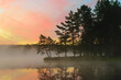 a wonderful sunrise picture with a gorgeous sky, fog covering the surface of the lake, black silhouettes of trees