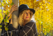 A Beautiful Woman Hugging A Tree In Autumn, Dressed In A Checkered Wool Shawl And A Black Hat.	