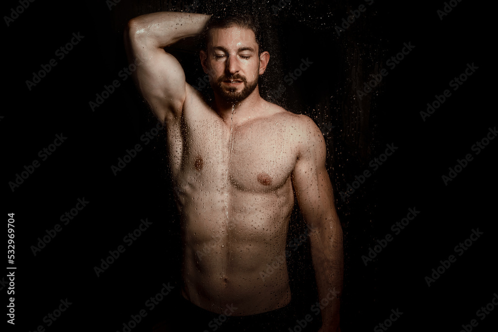handsome nude man stand in shower isolated on black wash his body under