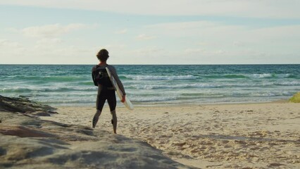 Wall Mural - Back view of the man wearing wetsuit walking with surfboard in his hands