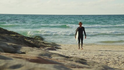 Wall Mural - Male surfer walking with his equipment during the summer day with wavy ocean