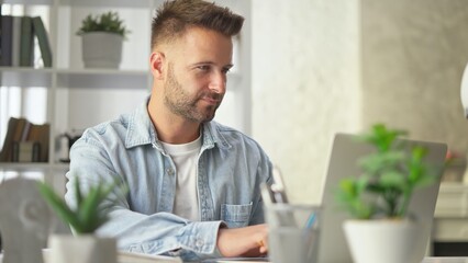 Poster - Happy businessman in casual using laptop in home office, Young adult man sitting at desk in study room, working online with computer, browsing the Internet, smiling.