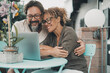 © simona - One couple middle age enjoy and have fun together using laptop sitting outdoor at the table in the garden at home. Man and woman in love and friendship doing video web call together smiling. Happiness