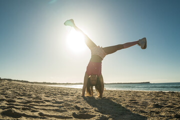 Wall Mural - Flexible girl in bright clothes standing at her hands on the sandy seashore