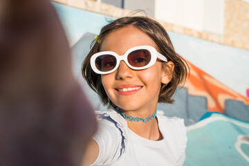 Brunette happy girl wearing sunglasses smiling toothy while making selfie outdoors