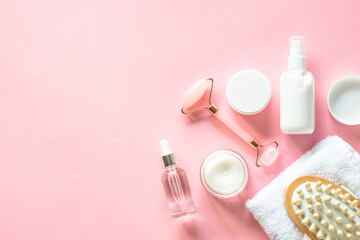 Poster - Natural cosmetics on pink. Skin care product, cream, soap serum, jade roller and white towel. Flat lay image with copy space.