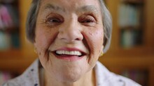 Happy, Smile And Senior Woman Face With Wisdom Against A Blurred Background In A Library. Portrait Of An Elderly Female Smiling In Retirement, Knowledge And Wise Happiness With A Positive Attitude
