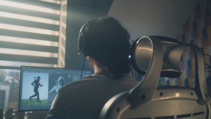 Poster - back view of man in headphones sitting at the table and creating video game hero and 3d animation in