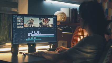 Poster - Male editor in headphones sitting at the table at night and editing video with astronauts for customer on pc in professional program while working remotely