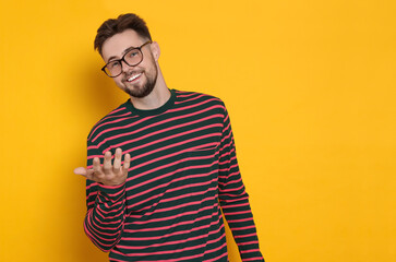 Wall Mural - Handsome man in striped sweatshirt gesturing on yellow background, space for text