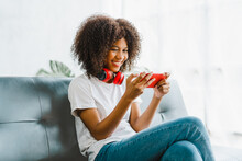 Excited Cheerful Gen Z Female Using Mobile Phone Getting Surprising Good News While Playing Mobile Game On Sofa.