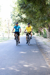 Young man and old cyclist having fun riding bicycle outdoors on countryside road
