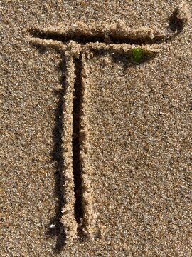On the beach in the sand is carved the letter T