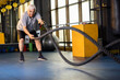 Active old man in sportswear training with battle rope in cross fit gym
