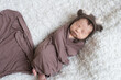 © capable97 - A cute little baby in a knitted hat with deer horns and a brown blanket sleeps on a white bouclé bedspread at home. Health and motherhood