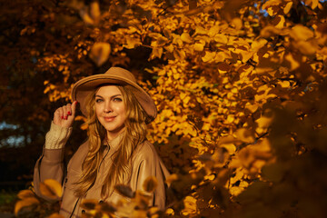 a beautiful woman in a hat and light clothes against the background of beautiful very trees in light clothes. Warm autumn. yellow leaves on the tree