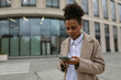 © Ivan Traimak - young african american woman businessman typing on a mobile phone against the backdrop of a business center in classic clothes