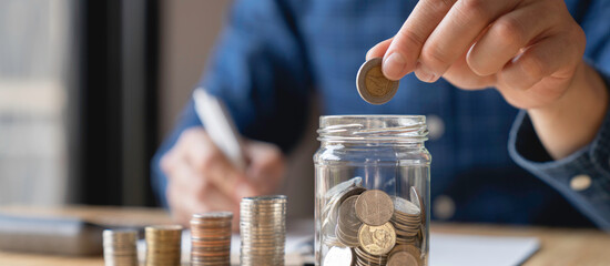 Tax and savings finance concept, businessmen saving money concept. hand holding coins and putting them in jug glass.