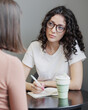 © MyJuly - Spanish woman psychologist or business coach conducts a session with a client and takes notes in a notebook. formation, change of activity. Mental health and psychological health support