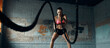 Concentrated young woman exercising with battle rope in gym