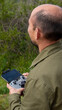 © Manuel Muñoz Acuña - Imagen de un hombre calvo de espalda pilotando un dron con control remoto en las manos, mirando el cielo y naturaleza de fondo con vegetacion verde