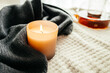 Leinwandbild Motiv Autumn decor. A burning candle next to a knitted woolen sweater and a pot of hot tea. Atmospheric, romantic mood