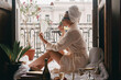 Beautiful young woman in bathrobe doing make-up while sitting between the room and balcony