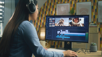 Poster - Woman in headphones editing video with astronauts for blog about space in professional software on computer, while sitting at the table at home and working remotely.
