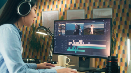 Poster - Concentrated asian woman sitting at the table and editing video for client in professional software using modern computer while working at home