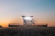 Front view of combine harvester working in a field at dusk with headlights turned on