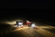 Illuminated field at night during the end of harvesting season: Aerial view of combine harvester discharging wheat grains
