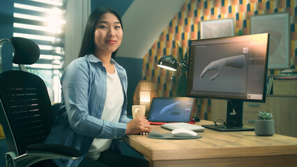 Poster - Female asian 3D designer sitting at the table near the modern computer and digital tablet, working on 3D project remotely from home and looking at camera.