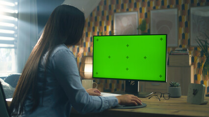 Poster - Asian woman sitting at the table and looking at screen of personal computer while working remotely from home or browsing the internet in free time. Freelance. Green screen and chromakey