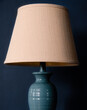 Light blue lamp with tan lampshade against a ark blue background