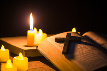 Light candle with holy bible and cross or crucifix on old wooden background in church.Candlelight and open book on vintage wood table christianity study and reading in home.Concept of christ religion