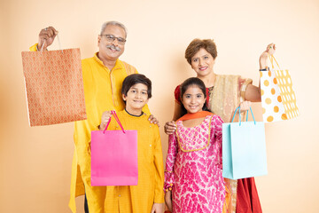 Wall Mural - Happy indian family wearing traditional cloths holding shopping bags and celebration diwali festival together isolated on studio background. Senior couple with kids celebrate festive season sale